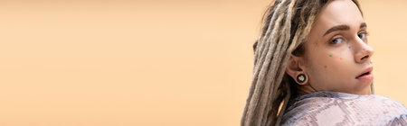 Young nonbinary person with dreadlocks looking at camera isolated on yellow, banner
