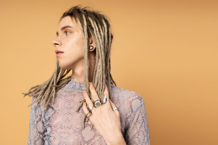 Stylish queer person touching dreadlocks isolated on yellowの写真素材