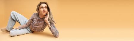 Young queer person in top and jeans lying on yellow background, banner