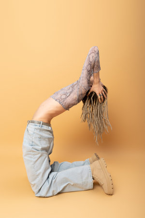 flexible queer person with dreadlocks posing on yellow background