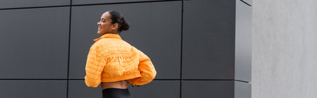 cheerful african american sportswoman in yellow puffer jacket exercising outside, bannerの写真素材