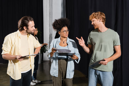 redhead man pointing with finger while talking to interracial students with screenplays in theater