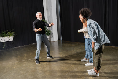 interracial actresses laughing near bearded art director posing and gesturing in theater. Translation of tattoo: om, shanti, peaceの写真素材