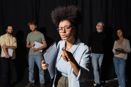 african american woman holding screenplay and gesturing during rehearsal near blurred actors and acting skills teacherの写真素材