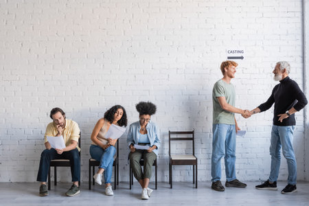 bearded producer shaking hands with redhead man near interracial actors. Translation of tattoo: kanji, dangerの写真素材