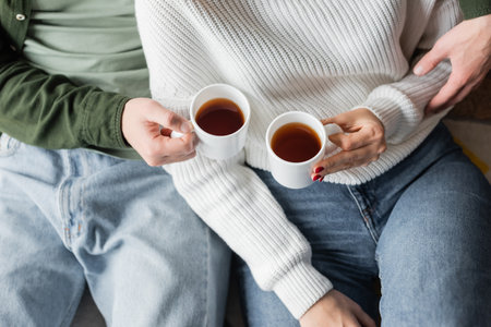 top view of cropped young couple in jeans holding cups with teaの写真素材