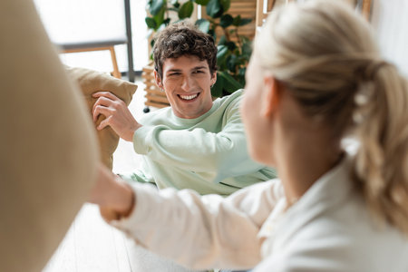 happy young man having pillow fight with girlfriend on blurred foregroundの写真素材