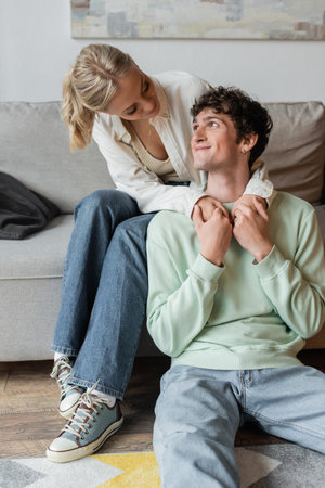 young and blonde woman embracing pleased man in living roomの写真素材