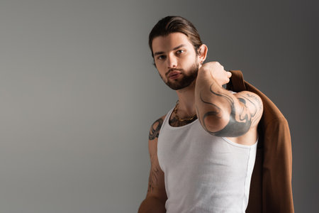 Portrait of stylish tattooed model in tank top holding jacket isolated on greyの写真素材
