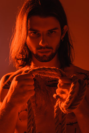 Portrait of tattooed man holding rope isolated on redの写真素材