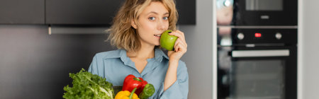 blonde young woman holding bowl with fresh vegetables and green apple in kitchen, bannerの写真素材