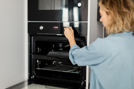 young woman with wavy hair using modern oven in kitchenの写真素材