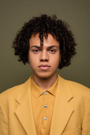front view of brunette african american man in yellow shirt and jacket looking at camera isolated on greyの写真素材