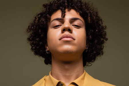 portrait of young african american man with curly hair looking at camera isolated on greyの写真素材