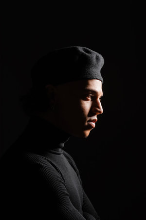 profile of african american man with shaded face wearing dark beret and sweater isolated on blackの写真素材