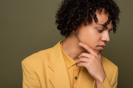 portrait of young african american man in yellow blazer holding hand near face isolated on greyの写真素材