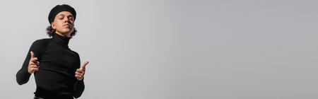 young african american man in stylish beret and black turtleneck looking at camera and showing finger gun gesture isolated on grey, bannerの写真素材