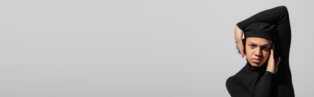 african american man in trendy beret and black turtleneck posing with hands near face isolated on grey, bannerの写真素材