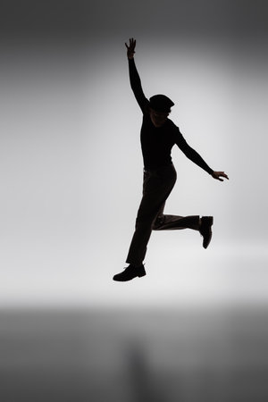dark silhouette of young african american man jumping on grey backgroundの写真素材