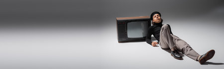 full length of african american man in black beret and trousers leaning on vintage tv set while...