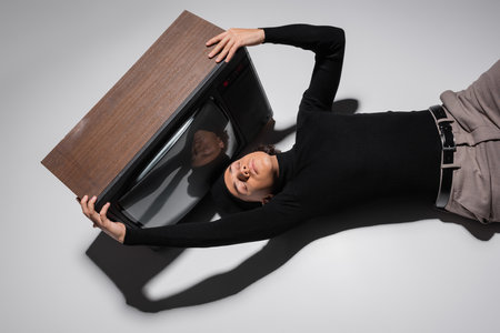 top view of fashionable african american man in black turtleneck and trousers lying near vintage tv...