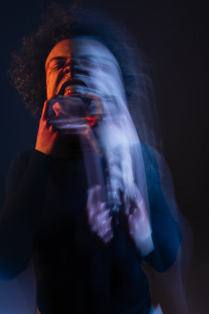 long exposure of wounded african american man with bipolar disorder and angry grimace on black with orange and blue lightの写真素材