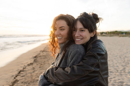 Smiling woman hugging friend on blurred beach during sunsetの写真素材