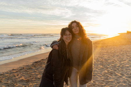 Curly woman hugging smiling friend on beach during sunset in Barcelonaの写真素材