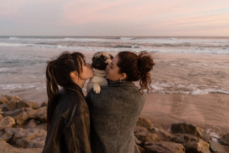 Friends kissing pug dog on beach in evening in Barcelonaの写真素材