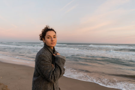 Young woman looking at camera while standing on beach in Barcelonaの写真素材