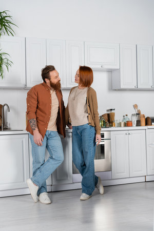 Smiling redhead woman looking at husband in kitchenの写真素材