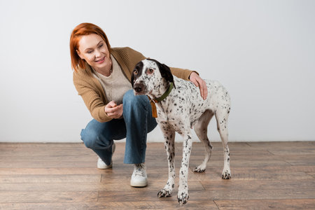Smiling red haired woman hugging dalmatian dog at home