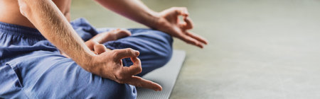 cropped view of man in blue pants sitting in lotus pose and doing gyan mudra, bannerの写真素材