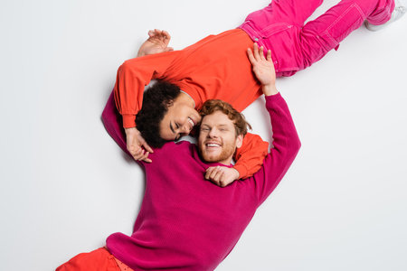 top view of happy redhead man and curly african american woman in magenta color clothes hugging each other on whiteの写真素材
