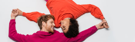top view of happy redhead man in magenta color clothes and curly african american woman holding...