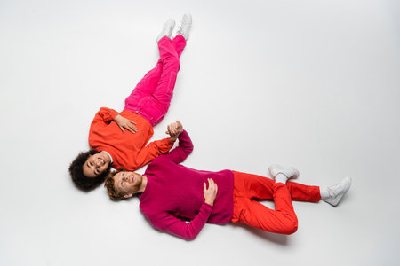 top view of joyful redhead man and curly african american woman in magenta color clothes lying on whiteの写真素材