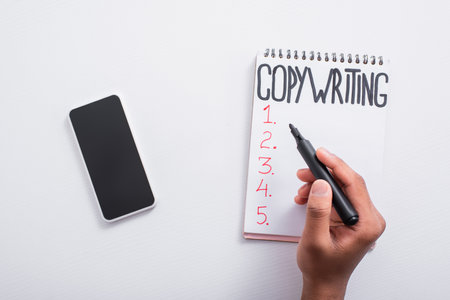 Top view of man holding marker near notebook with copywriting lettering and smartphone on table