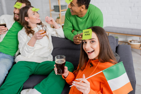 excited woman with king king word on sticky note holding Irish flag and glass of beer near...
