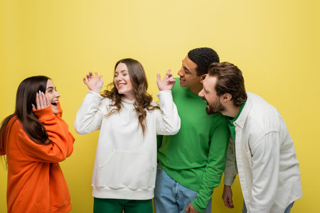 Smiling interracial people looking at friend on yellow backgroundの写真素材