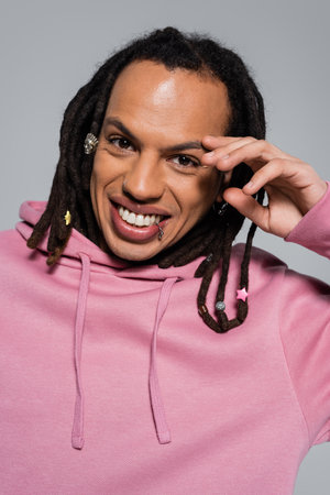 portrait of happy multiracial man in pink hoodie looking at camera isolated on grey