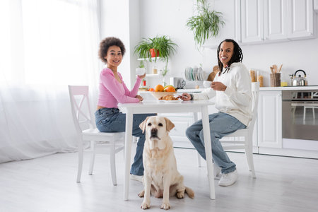 Smiling african american couple holding coffee near labrador in kitchenの写真素材