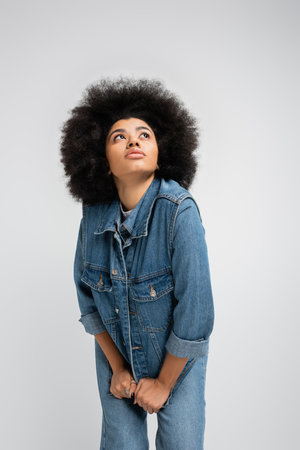 Curly african american woman in jeans and denim clothes looking up isolated on greyの写真素材