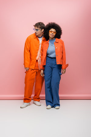 Full length of stylish interracial couple in sunglasses posing on pink backgroundの写真素材