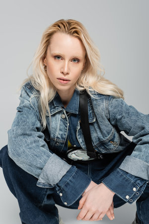 blonde albino woman in stylish denim jacket with belt bag posing isolated on greyの写真素材