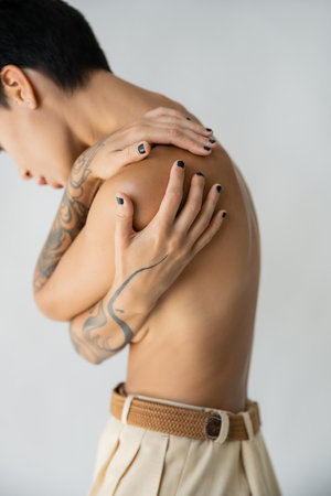 partial view of shirtless woman covering breast while hugging herself isolated on grey