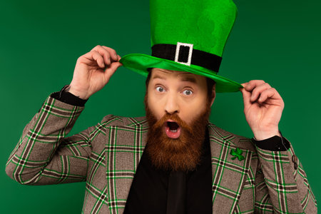 Shocked bearded man wearing hat with clover isolated on greenの写真素材