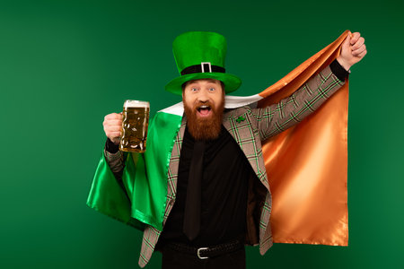 Excited man in hat holding glass of beer and Irish flag isolated on greenの写真素材