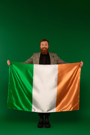 Full length of positive bearded man holding Irish flag on green backgroundの写真素材