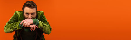 Adult man in green velvet jacket sitting on chair on red background, bannerの写真素材