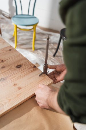 Cropped view of restorer measuring wooden board with calipers in workshop